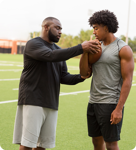 Football coach showing athlete how to hold a football.